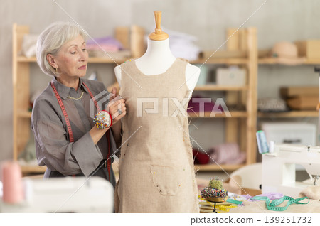 Mature female dressmaker working with mannequin in sewing workshop Mature female dressmaker working with mannequin in sewing workshop 139251732