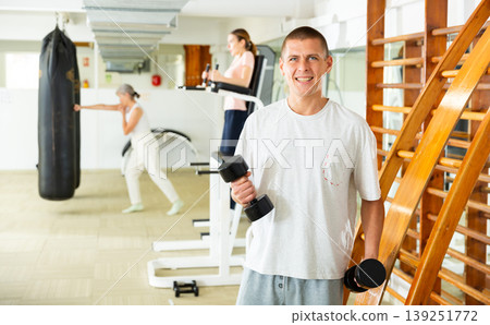 Smiling adult man exercising with dumbbells in gym Smiling adult man exercising with dumbbells in gym 139251772