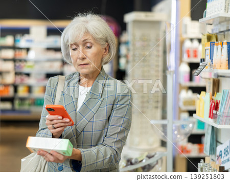 Mature woman scanning barcode on ointment package with her phone in pharmacy. Searching for information via Internet Mature woman scanning barcode on ointment package with her phone in pharmacy. Searching for information via Internet 139251803