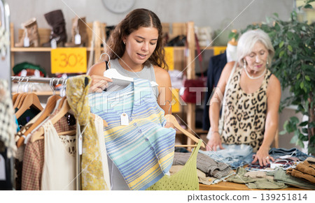 Positive young woman choosing something for summer in clothing store Positive young woman choosing something for summer in clothing store 139251814