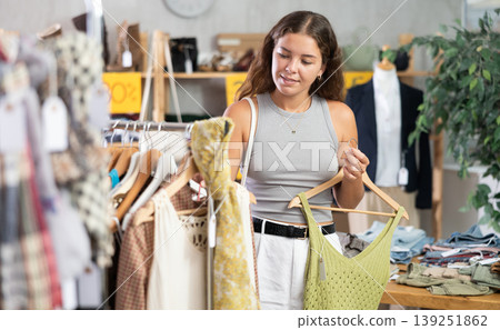 Positive young woman choosing something for summer in clothing store Positive young woman choosing something for summer in clothing store 139251862