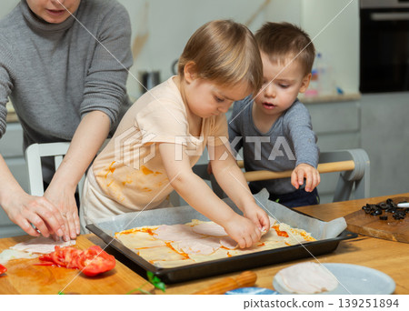 Family are cooking pizza together in cozy home kitchen. Cute kids with happy mother are preparing food or meal for dinner Family are cooking pizza together in cozy home kitchen. Cute kids with happy mother are preparing food or meal for dinner 139251894