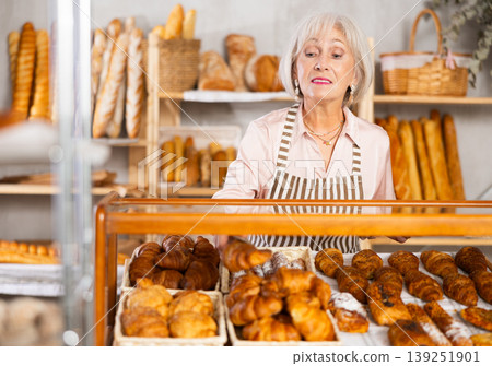 Elderly bakery saleswoman places fresh croissants on display Elderly bakery saleswoman places fresh croissants on display 139251901