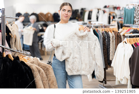 Young girl choosing short fur coat in clothing shop Young girl choosing short fur coat in clothing shop 139251905