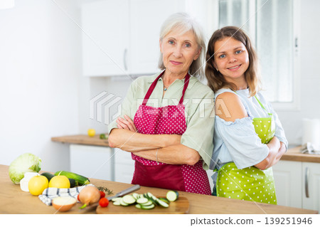Portrait of elderly woman and her daughter-in-law in an apron in the kitchen - cooking dinner together Portrait of elderly woman and her daughter-in-law in an apron in the kitchen - cooking dinner together 139251946