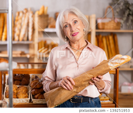 Elderly woman holds baguette wrapped in paper bag in bakery store 139251953