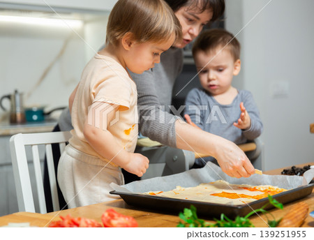 Family are cooking pizza together in cozy home kitchen. Cute kids with happy mother are preparing food or meal for dinner Family are cooking pizza together in cozy home kitchen. Cute kids with happy mother are preparing food or meal for dinner 139251955