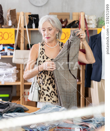 Attentive mature woman choosing trousers in clothing store Attentive mature woman choosing trousers in clothing store 139251999
