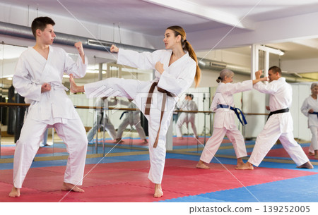 Teenage boy and woman sparring during group karate training Teenage boy and woman sparring during group karate training 139252005