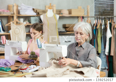 Two female dressmakers working with sewing-machine in tailor's workshop Two female dressmakers working with sewing-machine in tailor's workshop 139252017