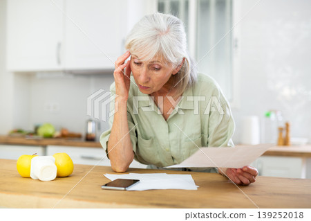 Worried mature woman checking papers at home Worried mature woman checking papers at home 139252018