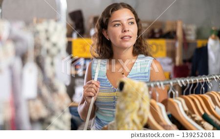 Young woman chooses a set of clothes for the summer. Visitor to the boutique examines new summer collection of clothes Young woman chooses a set of clothes for the summer. Visitor to the boutique examines new summer collection of clothes 139252081