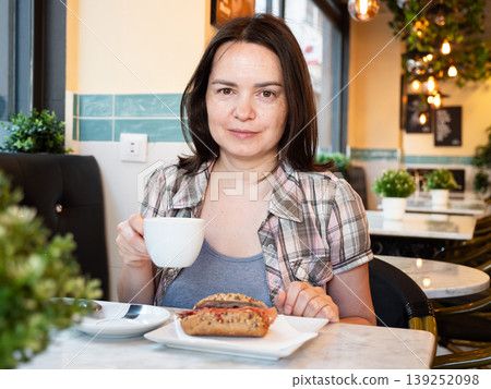 Young woman ordered breakfast - cup of coffee and sandwich with sausage products Young woman ordered breakfast - cup of coffee and sandwich with sausage products 139252098