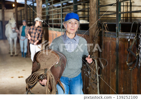 Female rancher carrying horse tack and saddle in horse farm Female rancher carrying horse tack and saddle in horse farm 139252100