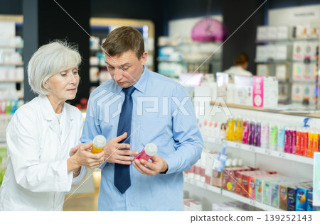 Senior woman pharmacist helps man buyer to decide on choice of lubricant. Senior woman pharmacist helps man buyer to decide on choice of lubricant. 139252143