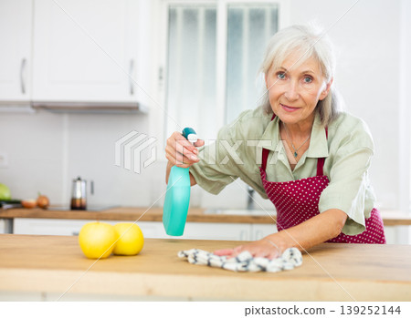 Mature woman cleaning kitchen table at home Mature woman cleaning kitchen table at home 139252144