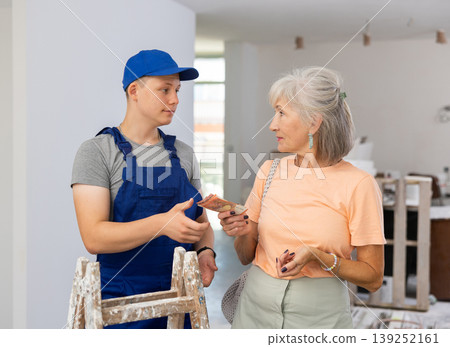 Senior woman paying wage to teenage boy assistant in construction site Senior woman paying wage to teenage boy assistant in construction site 139252161