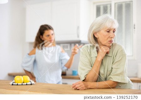 Quarrel of an elderly mother and adult daughter in the kitchen. Adult daughter is unhappy with elderly mother Quarrel of an elderly mother and adult daughter in the kitchen. Adult daughter is unhappy with elderly mother 139252170