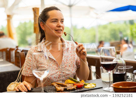 Woman eating hot dish of lamb in restaurant on an outdoor terrace Woman eating hot dish of lamb in restaurant on an outdoor terrace 139252181