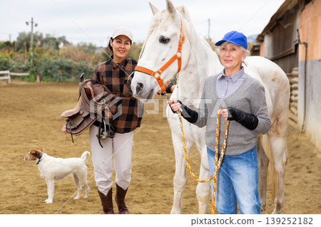 Women ranchers preparing white horse for ride Women ranchers preparing white horse for ride 139252182