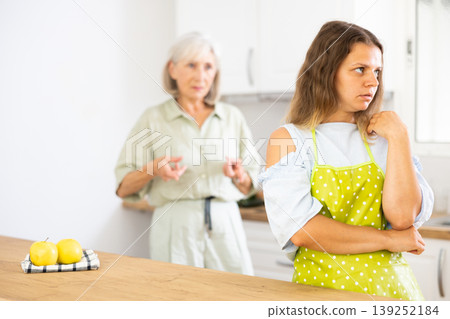 Senior woman scolding her adult daughter cooking breakfast in modern kitchen Senior woman scolding her adult daughter cooking breakfast in modern kitchen 139252184