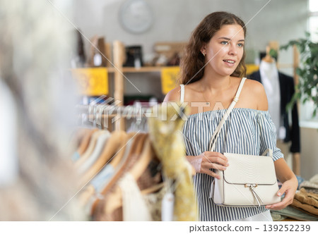 Happy young woman choosing handbag in clothing store Happy young woman choosing handbag in clothing store 139252239