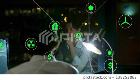 Contemplating office worker resting chin on hand at night office desk, with energy holograms 139252862