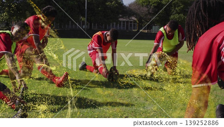 Stretching seven soccer players wearing red jerseys and colored bibs on grass field, with ball 139252886