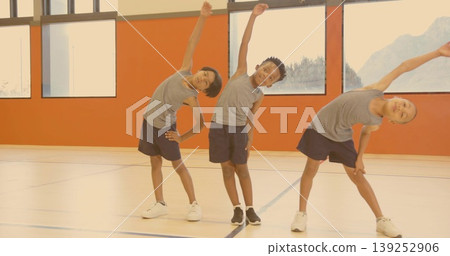Performing side bends three boys in matching athletic attire in school gym, with sports court lines Performing side bends three boys in matching athletic attire in school gym, with sports court lines 139252906