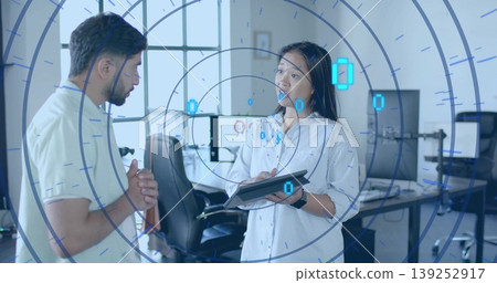 Discussing data trends two colleagues using tablet and monitors in tech office, with AR overlay Discussing data trends two colleagues using tablet and monitors in tech office, with AR overlay 139252917