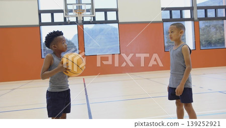 Two boys wearing matching gray uniforms playing basketball in gym court, with hoop and court lines Two boys wearing matching gray uniforms playing basketball in gym court, with hoop and court lines 139252921