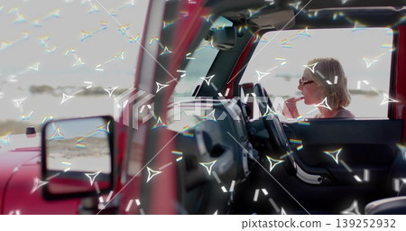 Applying lipstick blonde woman with sunglasses in red car at beach, mirror reflecting water Applying lipstick blonde woman with sunglasses in red car at beach, mirror reflecting water 139252932