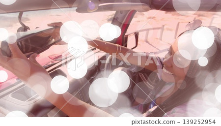 Reaching up woman wearing tank top adjusting rearview mirror in car by sandy roadside, copy space Reaching up woman wearing tank top adjusting rearview mirror in car by sandy roadside, copy space 139252954
