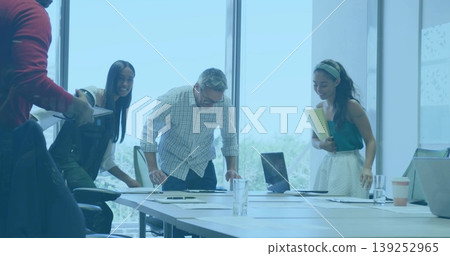Leaning colleagues in formal attire reviewing documents on conference table, with laptop and tablet Leaning colleagues in formal attire reviewing documents on conference table, with laptop and tablet 139252965