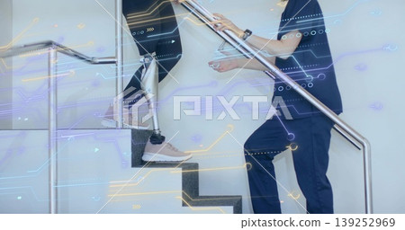 Ascending patient on prosthetic leg climbing therapy stairs with therapist in scrubs, handrails 139252969