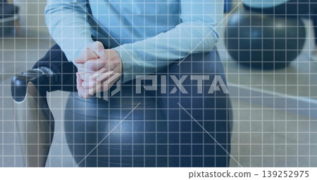 Sitting woman in blue top clasping hands while balancing on ball in gym, with bike handle Sitting woman in blue top clasping hands while balancing on ball in gym, with bike handle 139252975