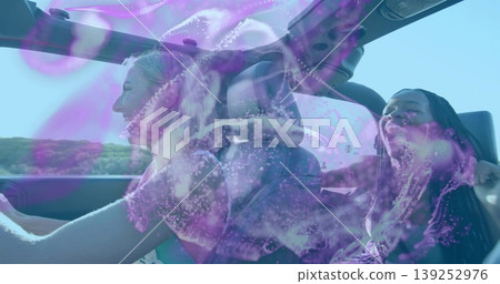 Two friends driving convertible with open sunroof on coastal road, purple holograms on windshield Two friends driving convertible with open sunroof on coastal road, purple holograms on windshield 139252976