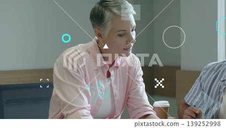 Mature woman in pink shirt reviewing documents, leaning at conference table with coffee cup and pen 139252998