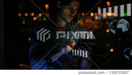 Tapping tablet man in plaid shirt projecting digital data visualizations on window in dark office Tapping tablet man in plaid shirt projecting digital data visualizations on window in dark office 139253007
