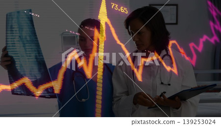 Analyzing X-ray, nurse in scrubs, doctor in coat taking notes in exam room, financial graph overlay Analyzing X-ray, nurse in scrubs, doctor in coat taking notes in exam room, financial graph overlay 139253024