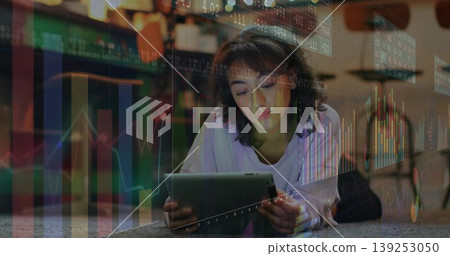 Holding tablet woman studying financial trends lying on carpeted floor at home, with data overlays Holding tablet woman studying financial trends lying on carpeted floor at home, with data overlays 139253050