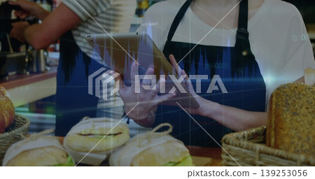 Holding tablet, employee serving bagels and sandwiches at cafe counter, with baskets, portafilter Holding tablet, employee serving bagels and sandwiches at cafe counter, with baskets, portafilter 139253056