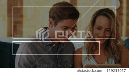Smiling couple in denim shirt and sleeveless top leaning on sofa in living room, viewing tablet Smiling couple in denim shirt and sleeveless top leaning on sofa in living room, viewing tablet 139253057