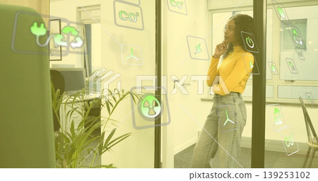 Woman in mustard top analyzing sustainability icons on glass partition in meeting room, copy space Woman in mustard top analyzing sustainability icons on glass partition in meeting room, copy space 139253102