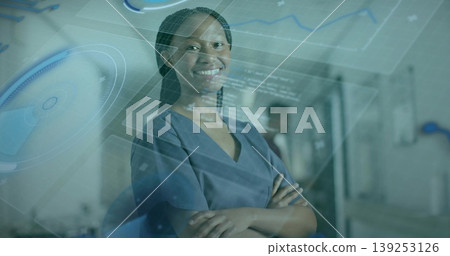 Standing nurse wearing scrubs crossing arms in medical corridor, with digital chart overlays Standing nurse wearing scrubs crossing arms in medical corridor, with digital chart overlays 139253126