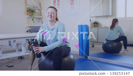 Sitting woman with prosthetic leg holding water bottle on ball in clinic, wearing sportswear Sitting woman with prosthetic leg holding water bottle on ball in clinic, wearing sportswear 139253147