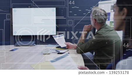 Reviewing manager in olive-green shirt examining documents in meeting room with display, coffee mug Reviewing manager in olive-green shirt examining documents in meeting room with display, coffee mug 139253178