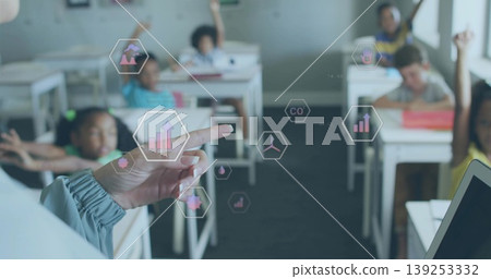 Pointing teacher's hand interacting with hexagonal icons in classroom, with students raising hands Pointing teacher's hand interacting with hexagonal icons in classroom, with students raising hands 139253332