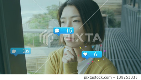 Gazing woman wearing mustard cardigan leaning on glass door on balcony, with floating social icons Gazing woman wearing mustard cardigan leaning on glass door on balcony, with floating social icons 139253333
