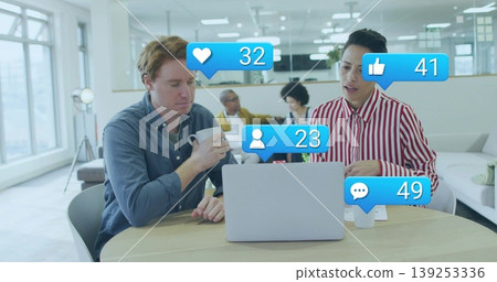 Reviewing two colleagues sitting at round table in lounge, with laptop coffee social media icons Reviewing two colleagues sitting at round table in lounge, with laptop coffee social media icons 139253336
